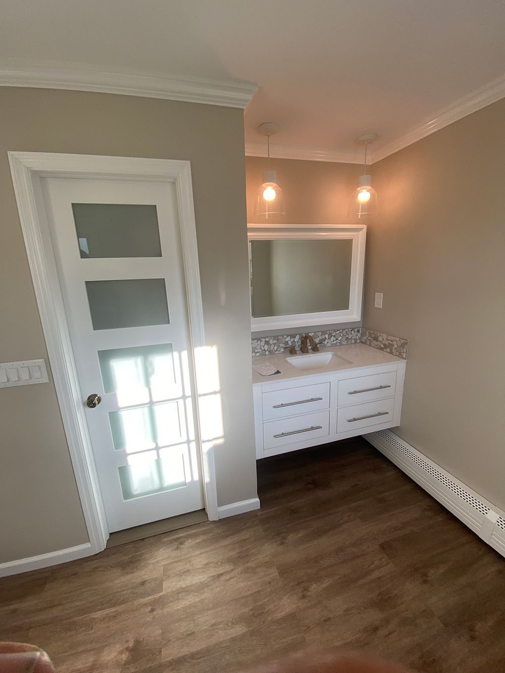 Bathroom with white floating vanity, large mirror, door, and wood-look flooring. Beige walls.