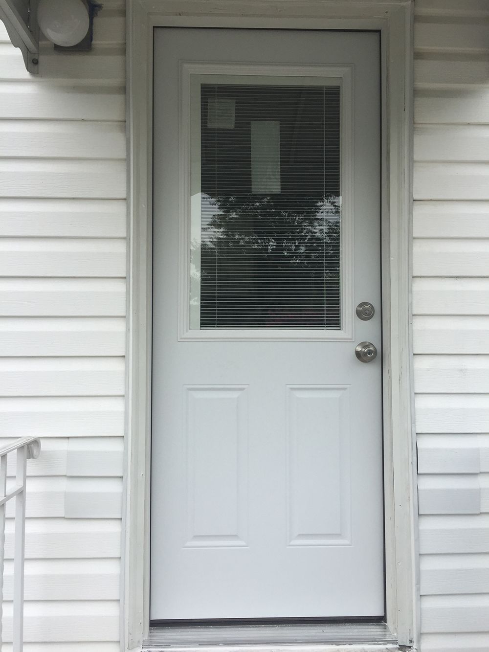 White door with window and blinds in a white-sided building.