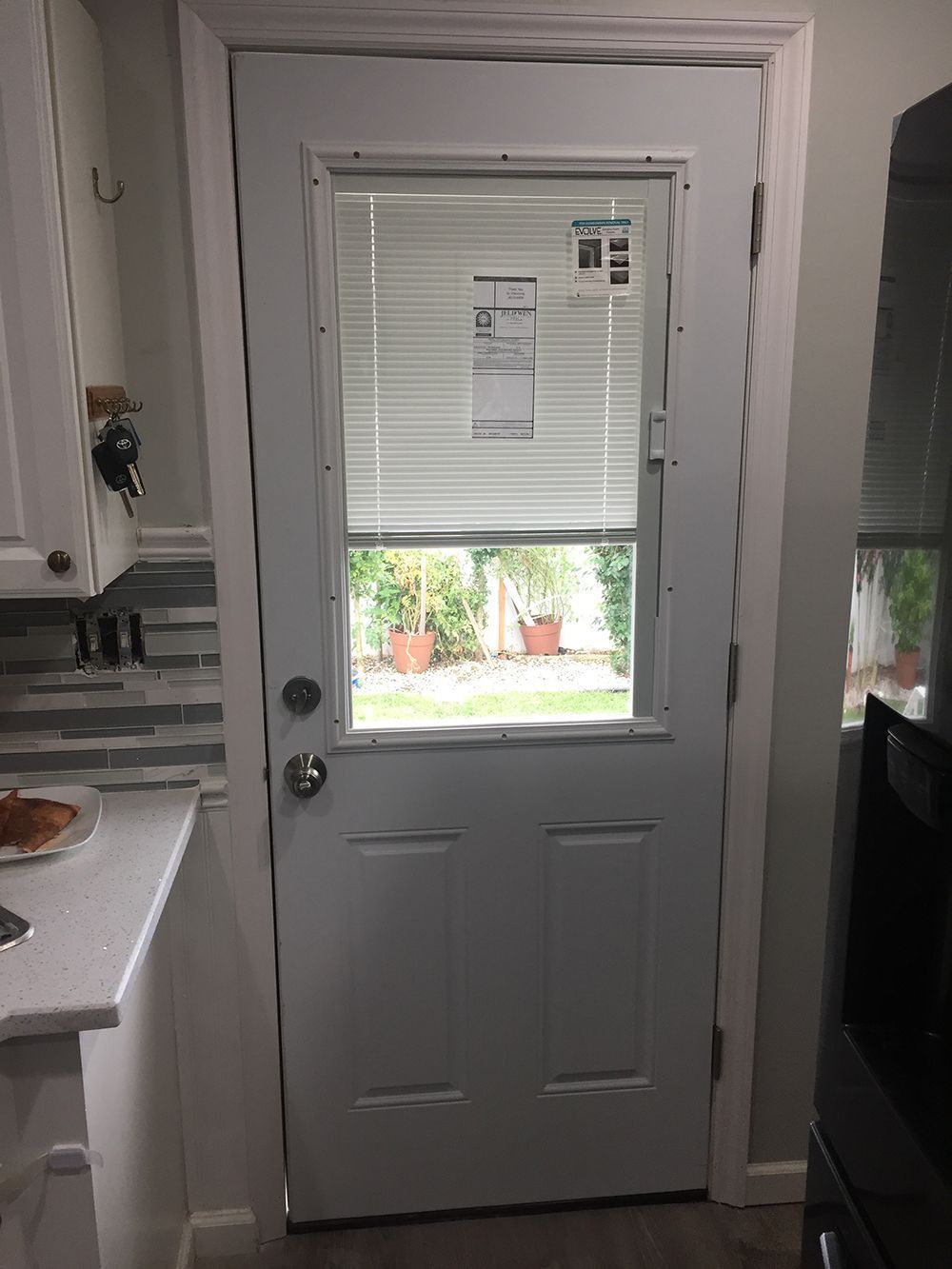 White kitchen door with window and blinds. View into a backyard.
