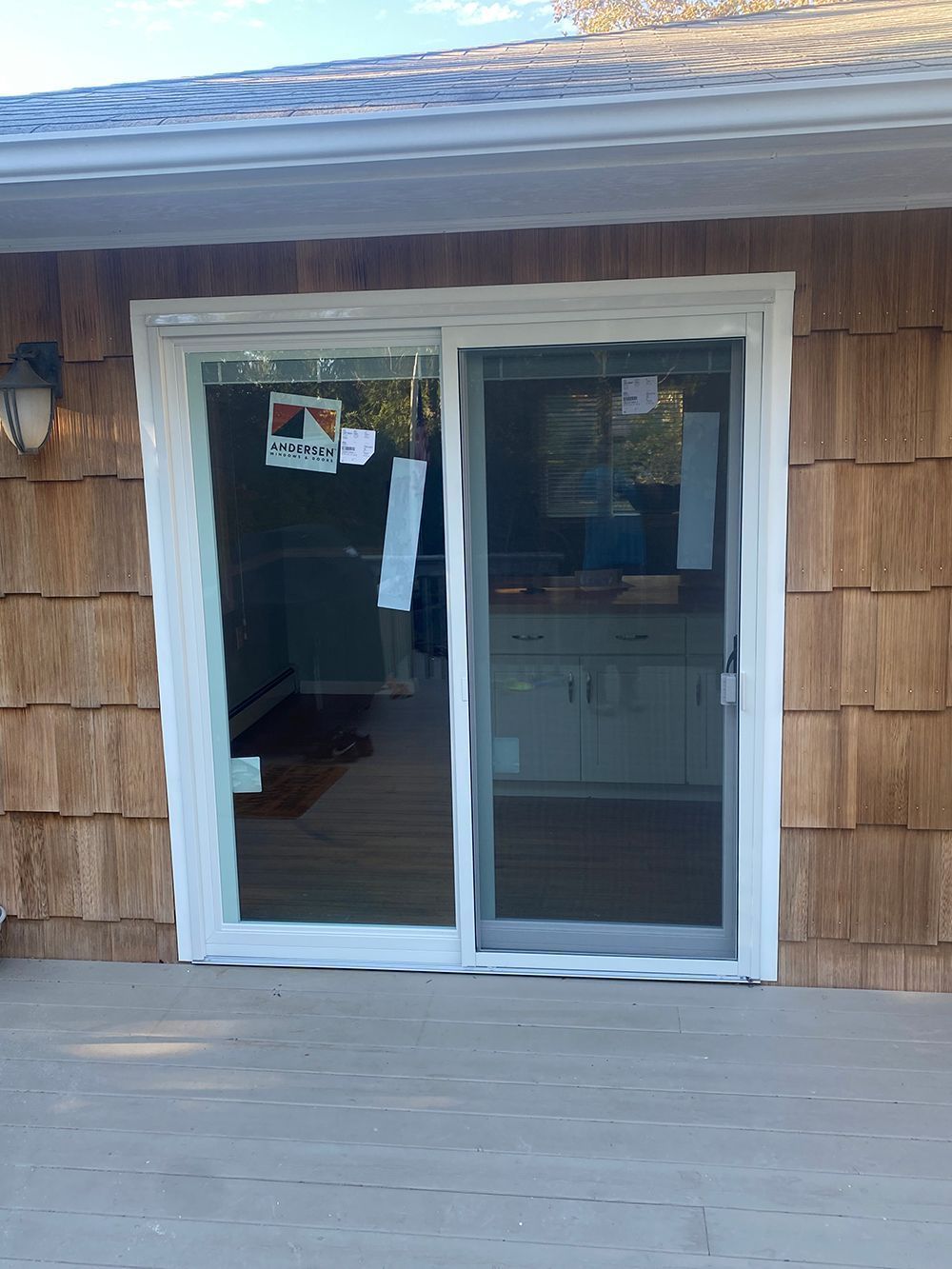Sliding glass doors with white frame, on wood deck, cedar shingle siding.