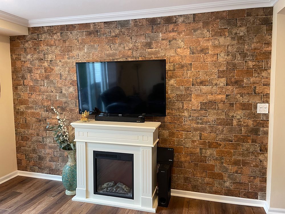 TV mounted on a brick-look wall above a white fireplace. Room with hardwood floors and crown molding.