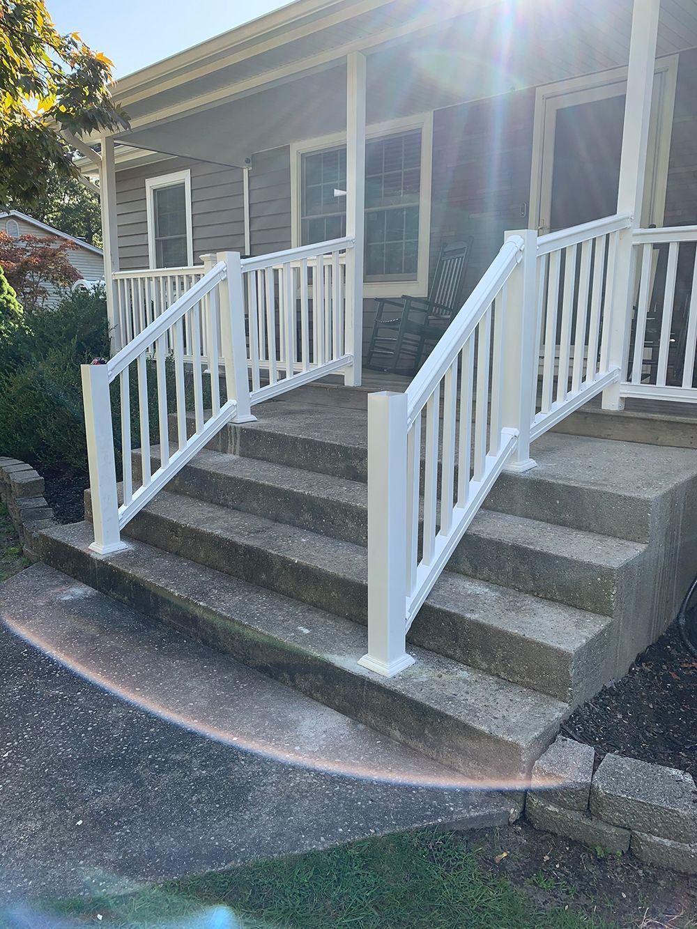 White railing on concrete steps leading to a gray house porch; sunny day.