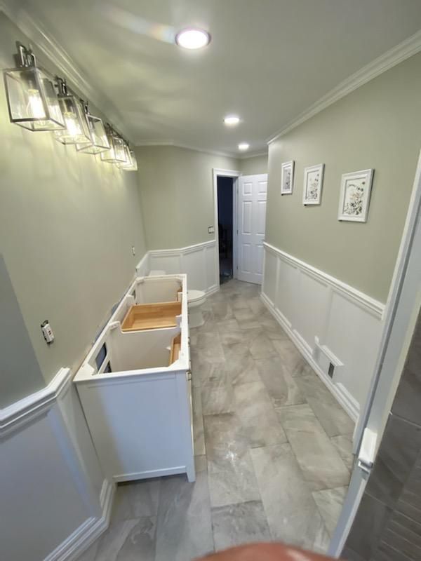 Bathroom under renovation with gray walls, white cabinets, and trim, with a gray tile floor.
