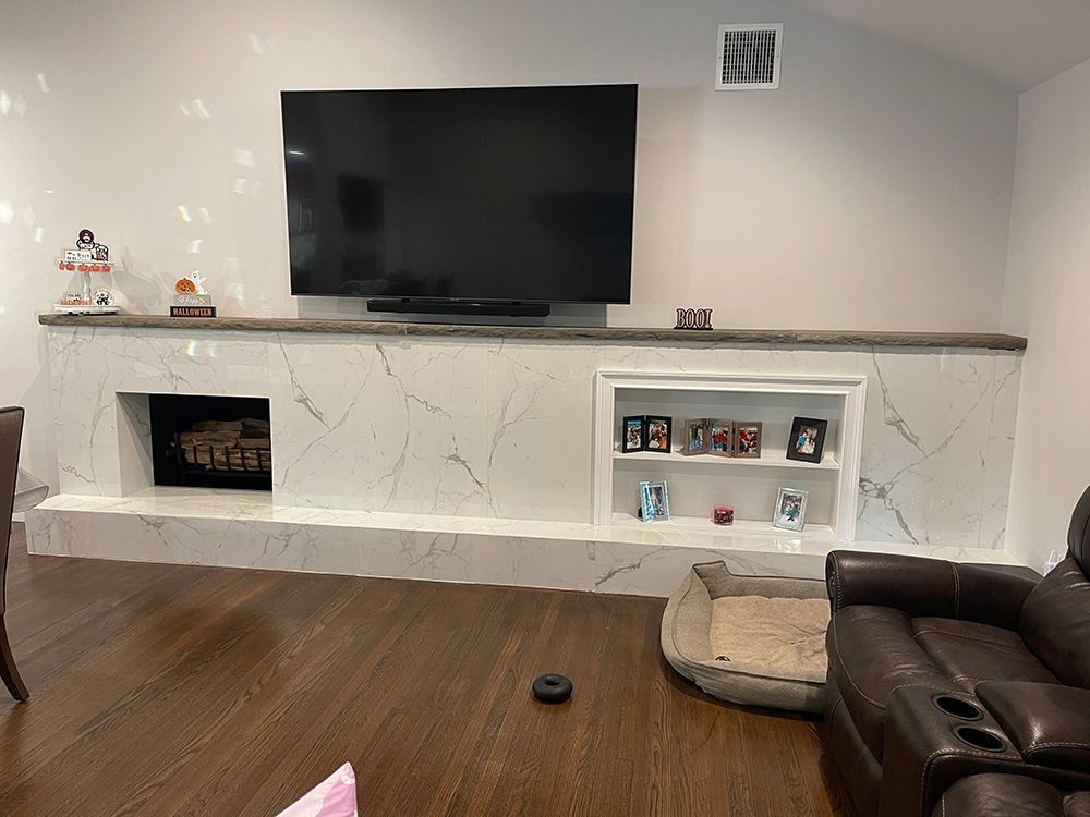Living room with fireplace, TV above. White stone mantel with shelf, built-in shelving, brown sofa and floor.