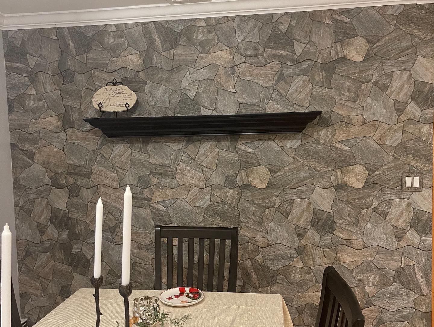A dining room with a stone accent wall, a dark wooden shelf, and a table set for a meal.
