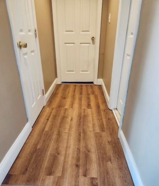 Narrow hallway with wood-look flooring, white doors and trim, and tan walls.