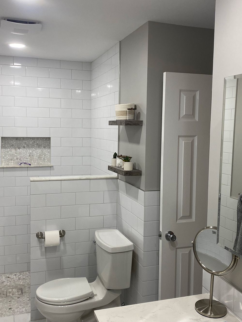 Bathroom with white subway tile, toilet, shelves with décor, and a white door.