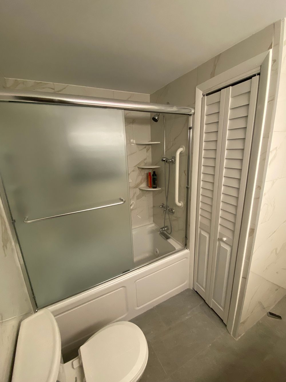 Bathroom with a shower/tub, frosted glass door, and a toilet. White and grey tones.