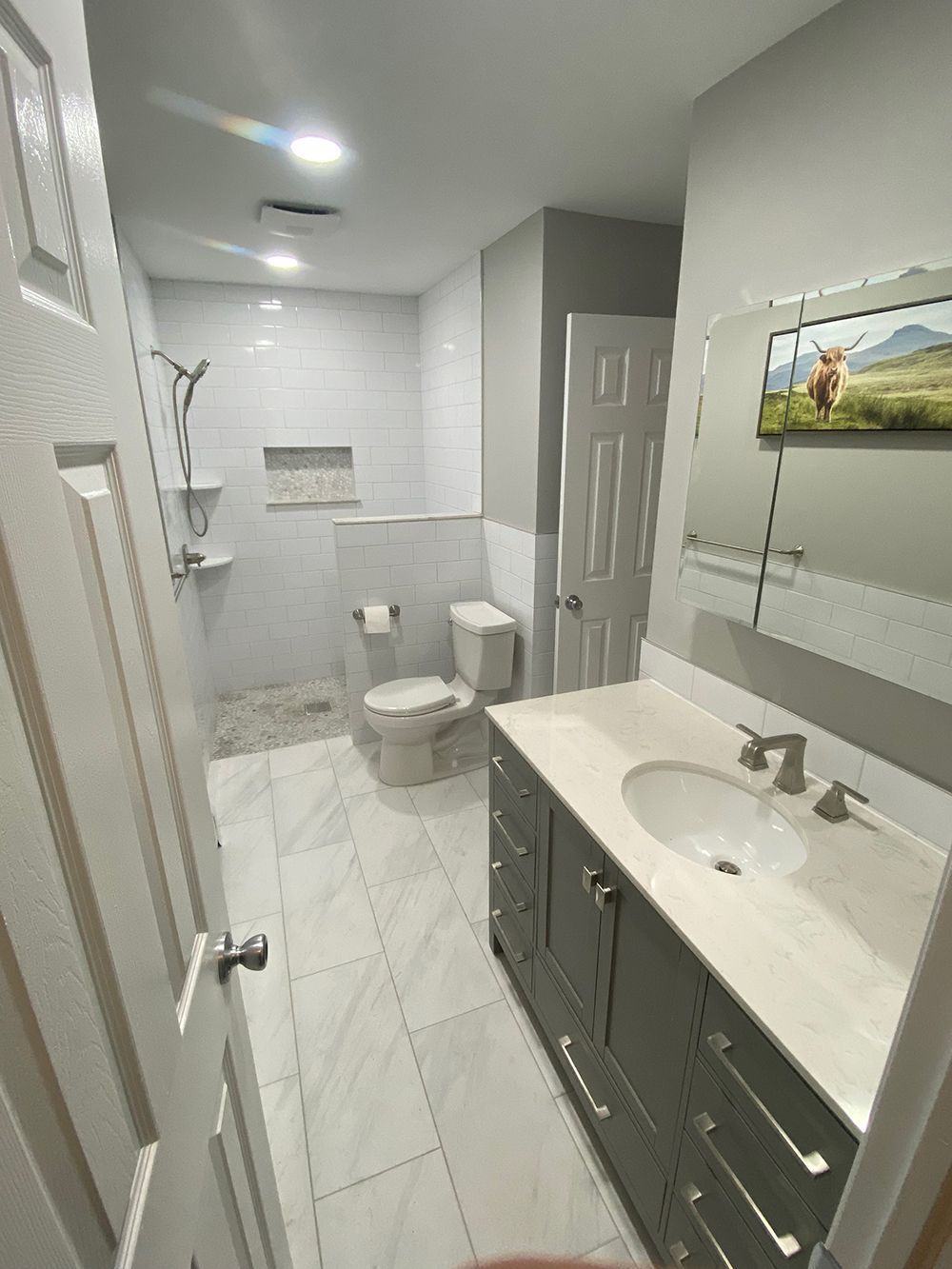Bathroom with gray vanity, white tiles, shower, toilet, and artwork.