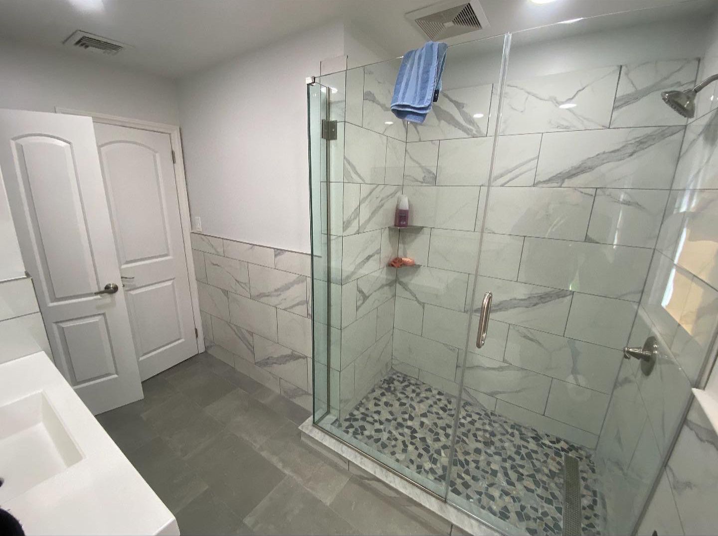 Bathroom with glass shower door, marble tile walls and floor, white door and vanity.