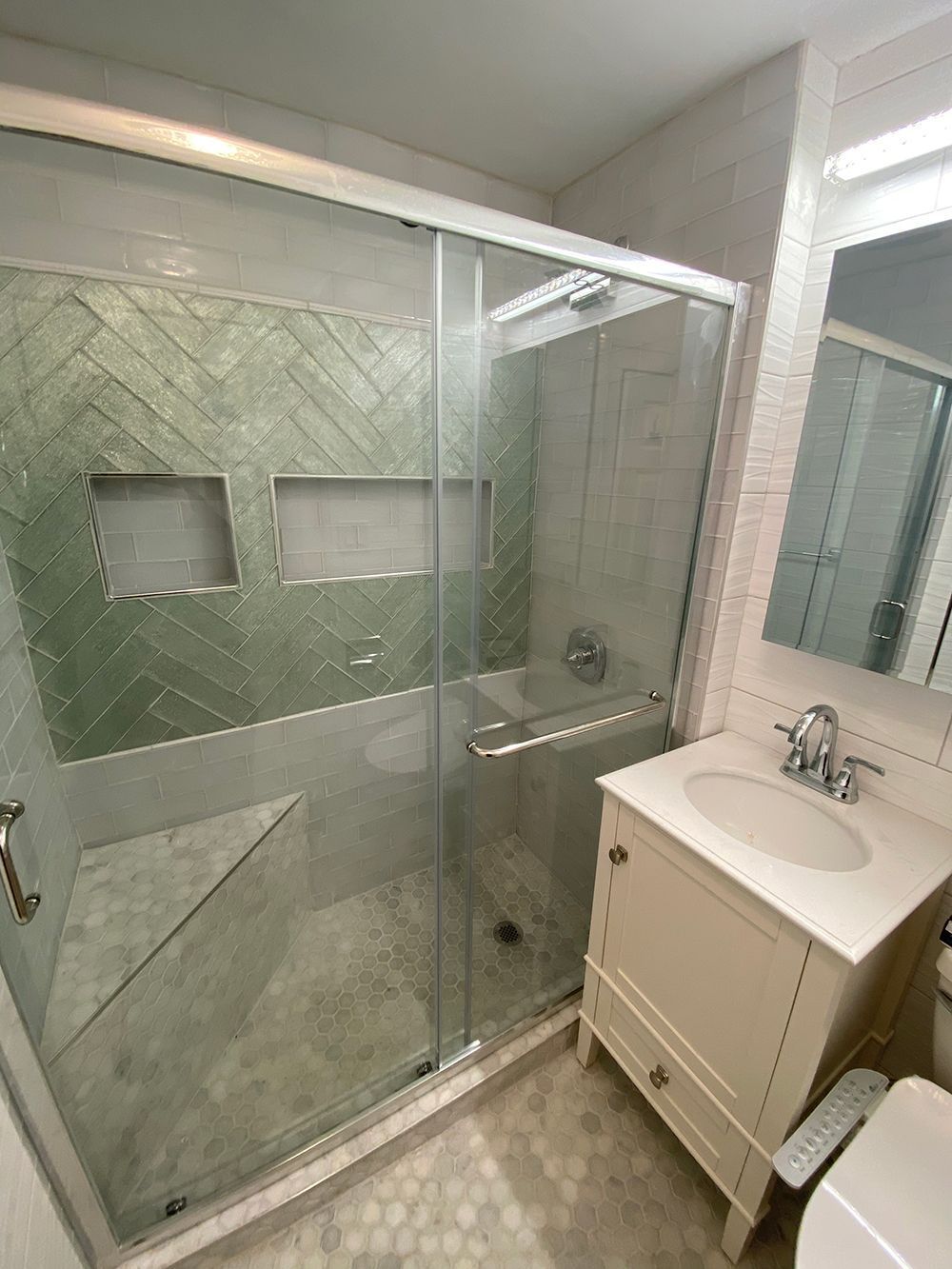 Bathroom with glass shower, green tiled wall, white vanity, and marble floor.