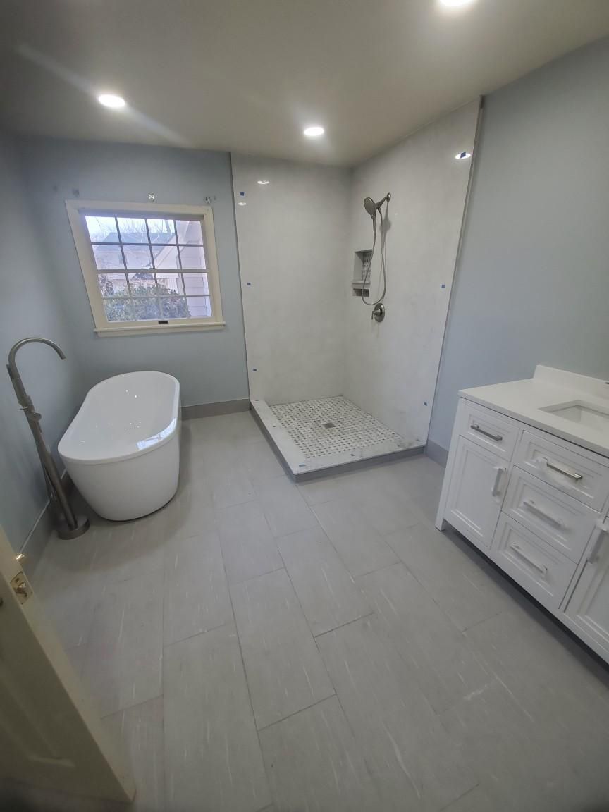 Bathroom with a white freestanding tub, shower, vanity, and light blue walls.