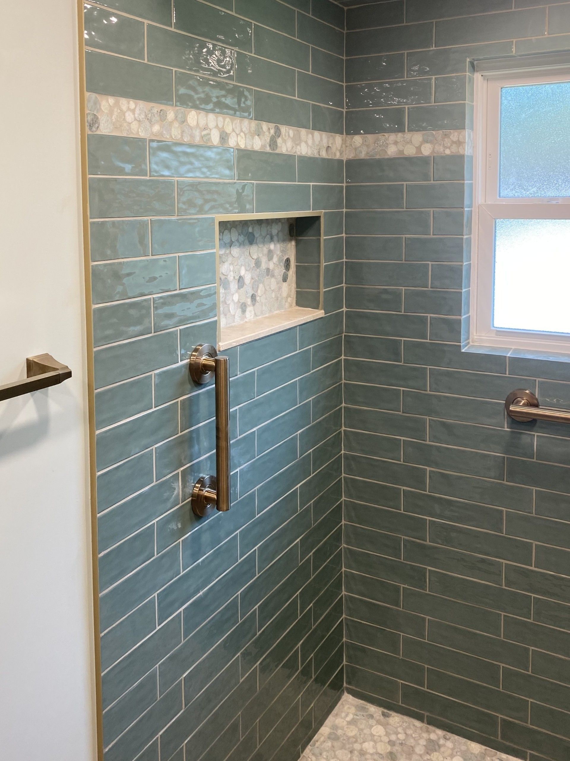 Bathroom with teal subway tile, silver accent, shower niche, and grab bars.