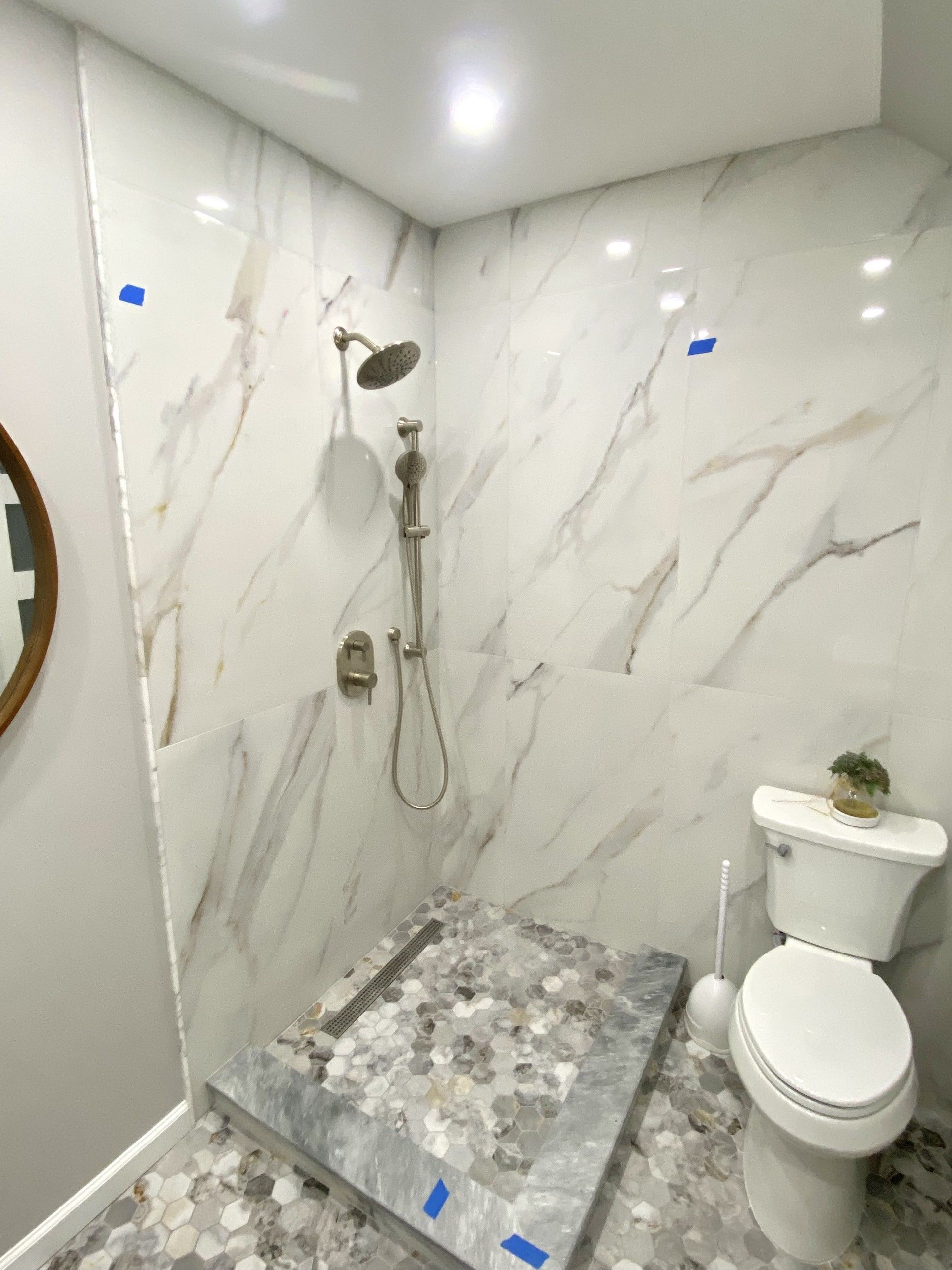 Bathroom with white marble tile shower, pebble floor, and white toilet.