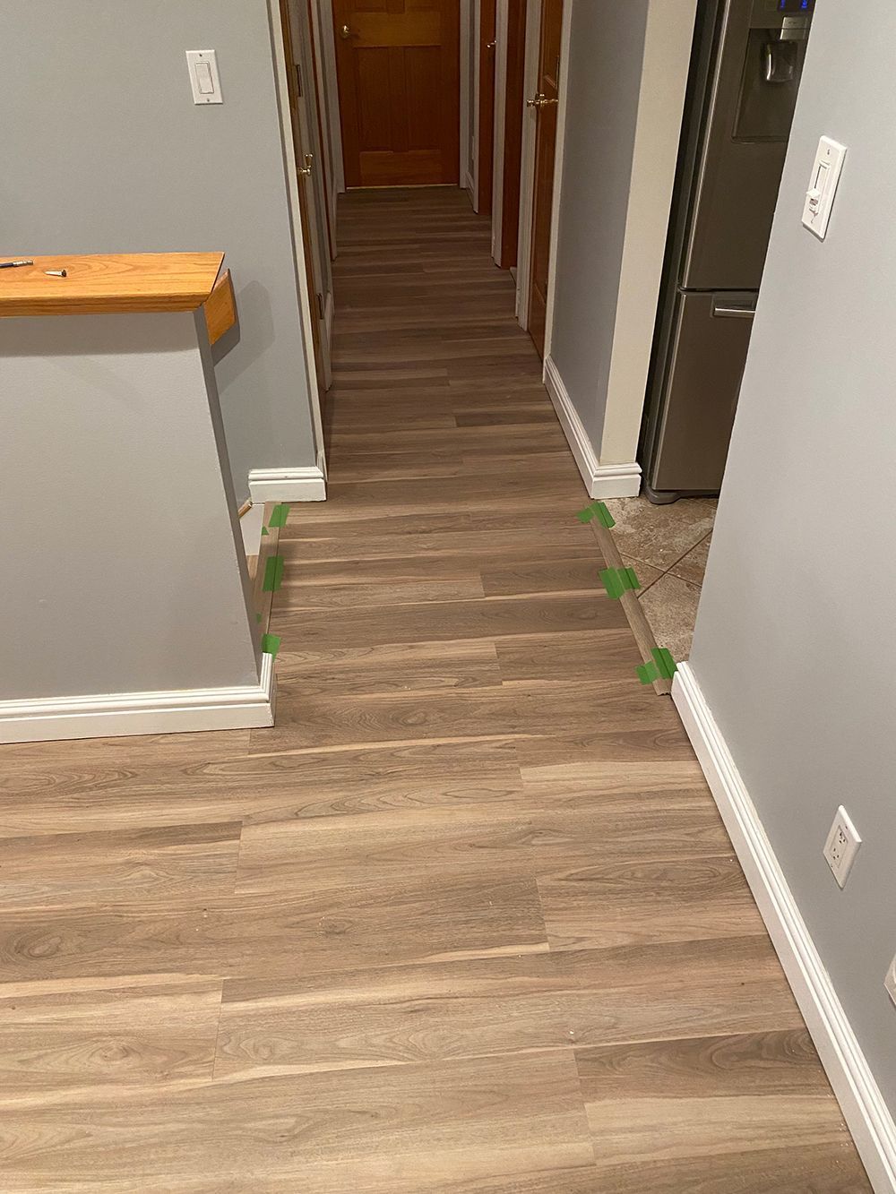 Hallway with wood-look flooring, gray walls, white baseboards, and a view towards a closed door.