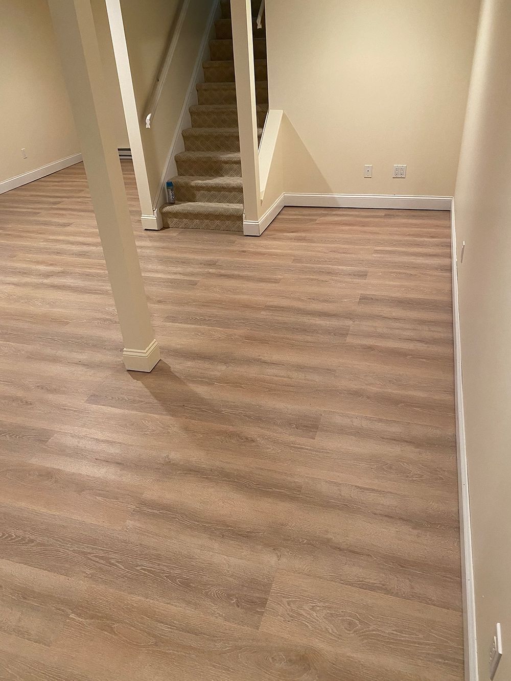 Basement with wood-look flooring, beige walls, and staircase.