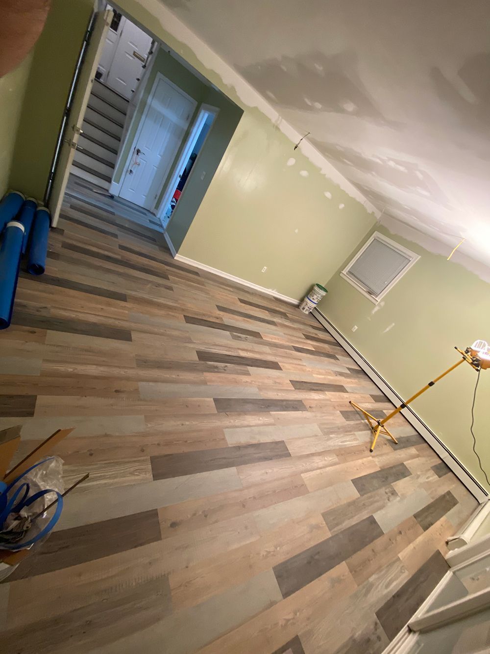 Room with new wood-look flooring, green walls, unfinished ceiling, and a doorway leading to stairs.