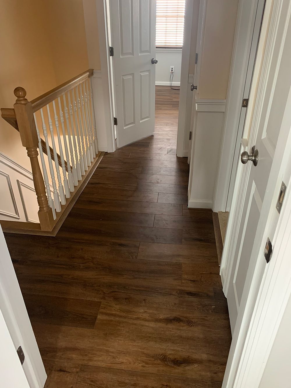 Hallway with dark wood-look flooring and white doors. A staircase with a wood handrail is visible on the left.
