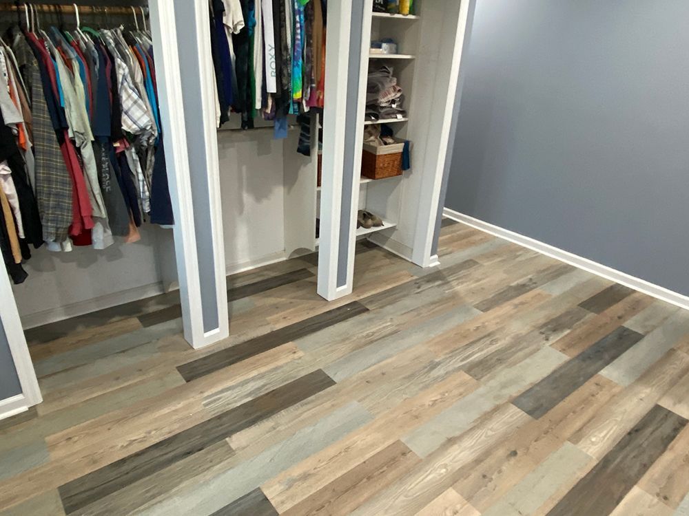 Closet with clothes on hangers and new wood-look flooring. Light and dark wood planks on floor. Gray wall.