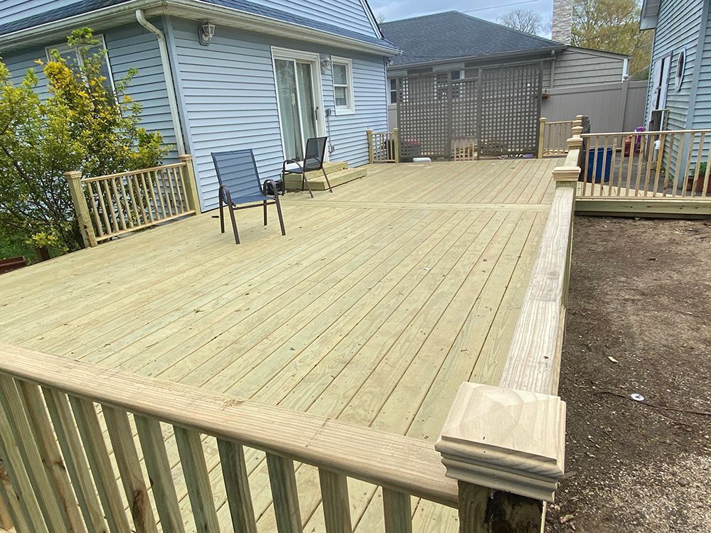 Wooden deck attached to a light blue house, with railings and two chairs.