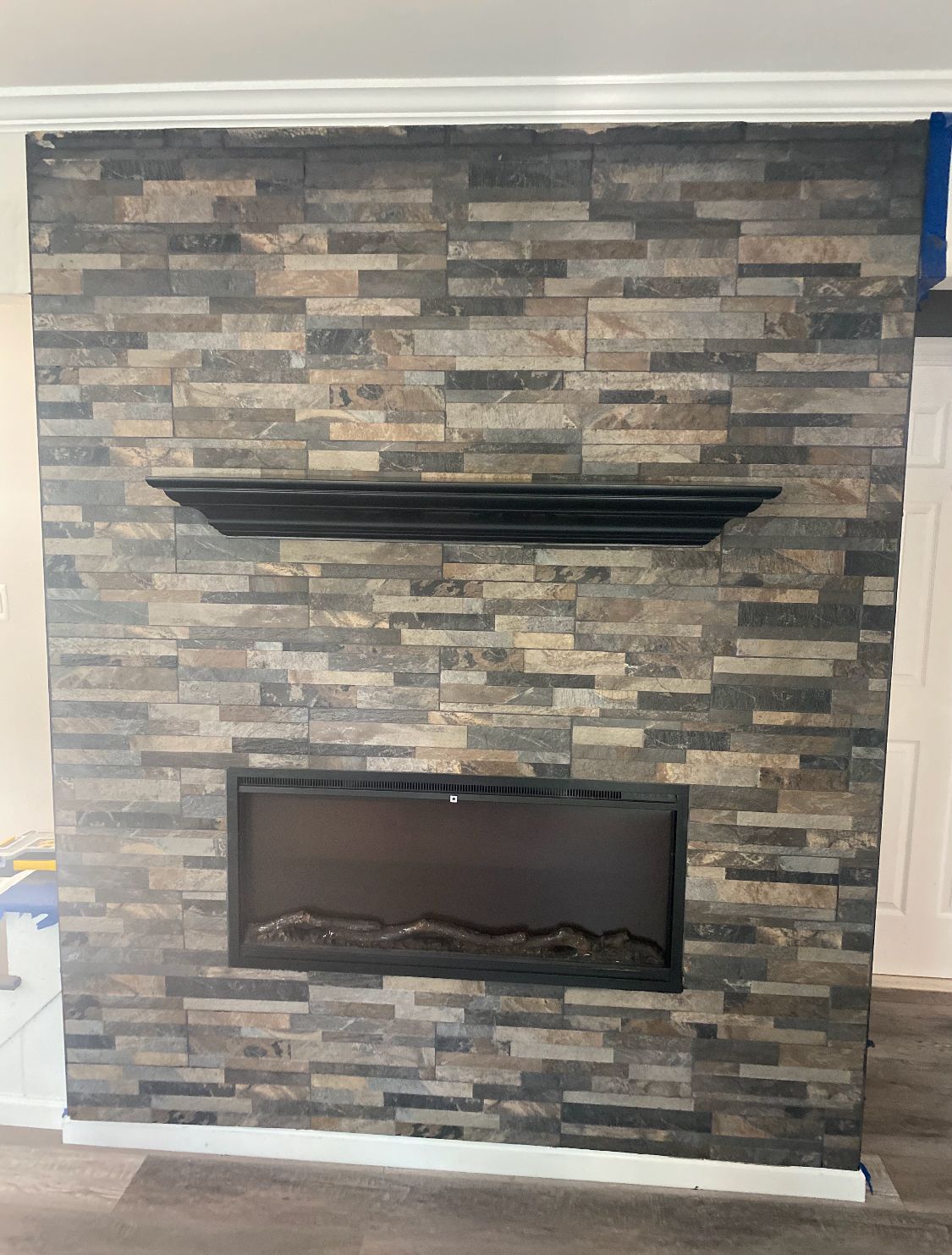 Fireplace with gray stacked stone, black fireplace insert, and black mantel.