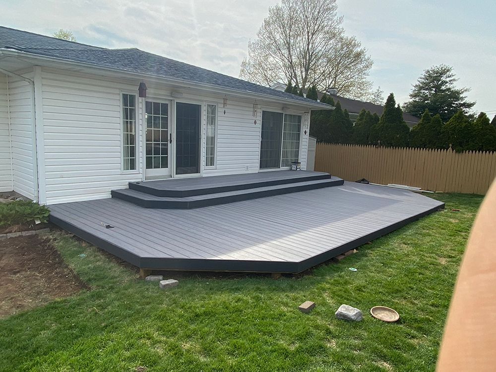 A gray composite deck with steps leads to white house with glass doors. The deck sits on green grass.