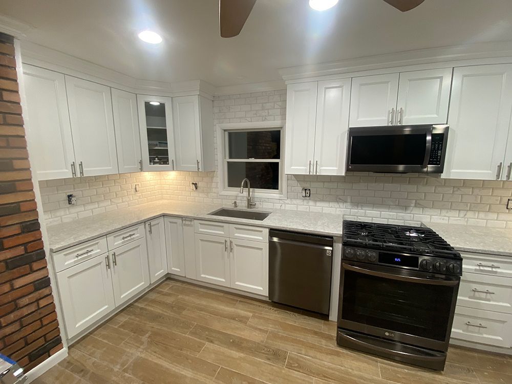 White kitchen with cabinets, appliances, countertops, and a brick wall.