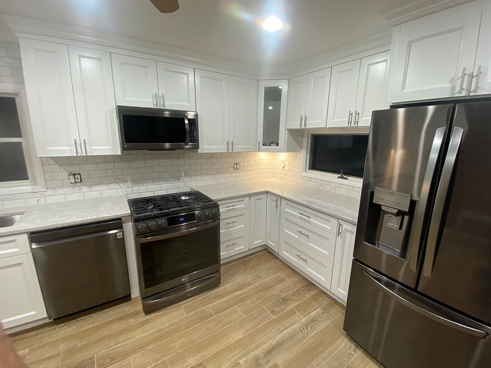 White kitchen with stainless steel appliances and light wood floors.