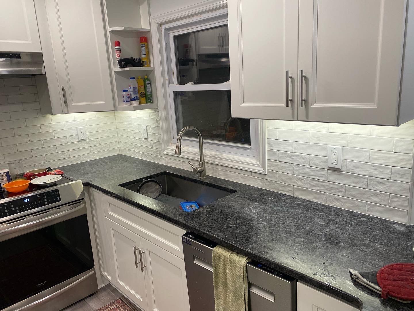 Kitchen with white cabinets, dark countertop, stainless steel sink, and stove.