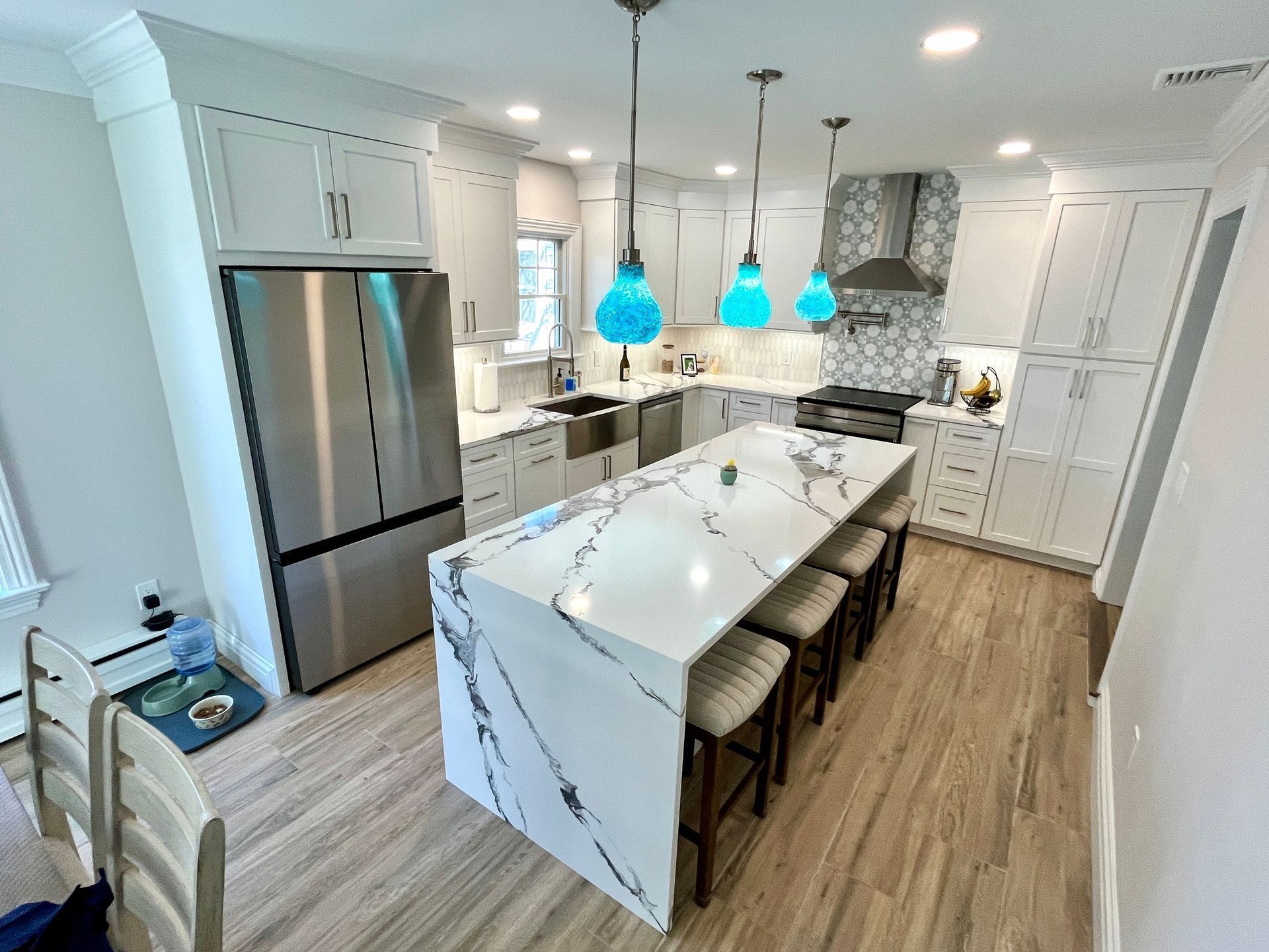 Modern white kitchen with island, stainless steel appliances, and turquoise pendant lights.