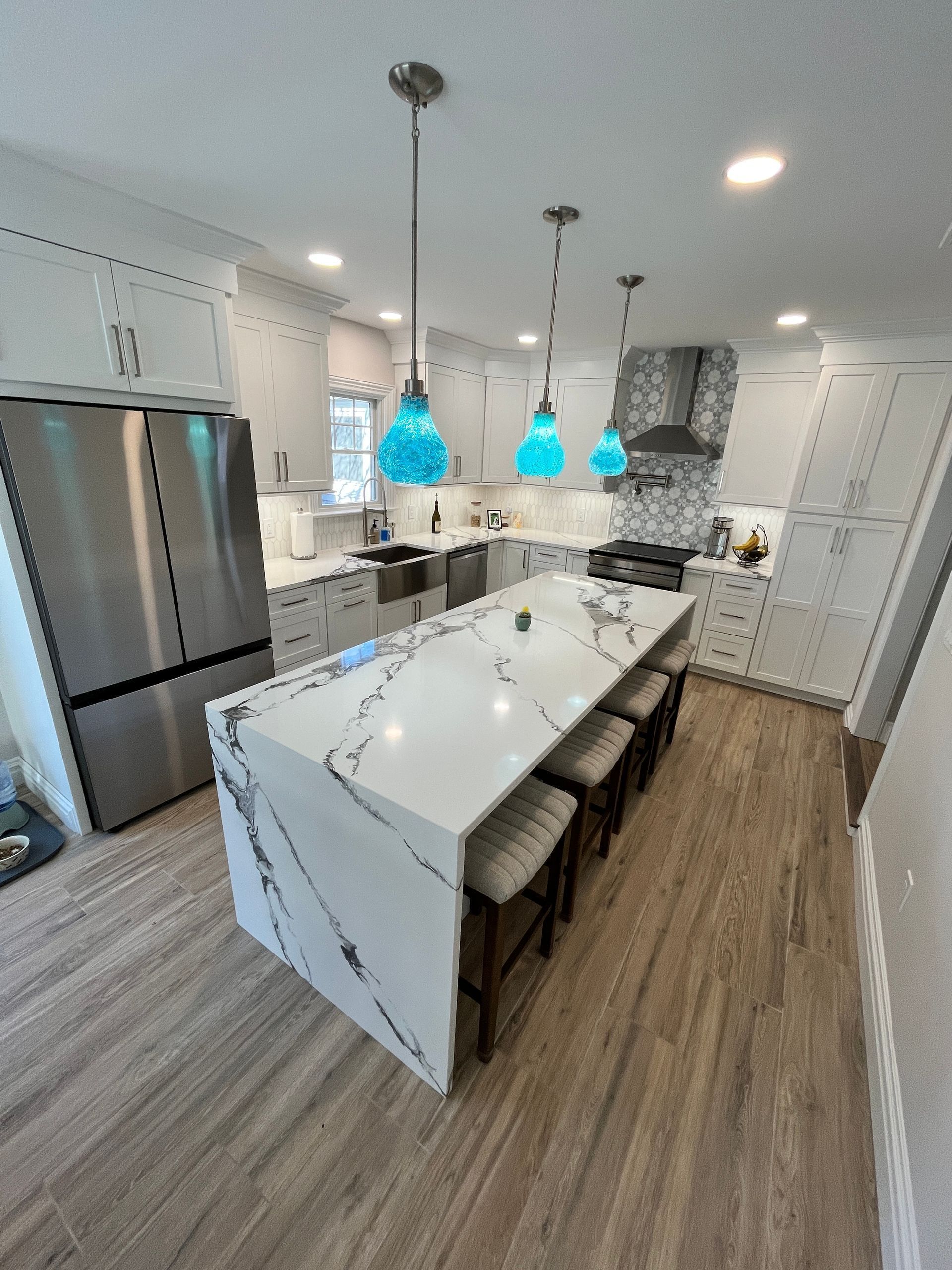 Modern kitchen with white cabinets, quartz countertops, and blue glass pendant lights over an island with bar stools.