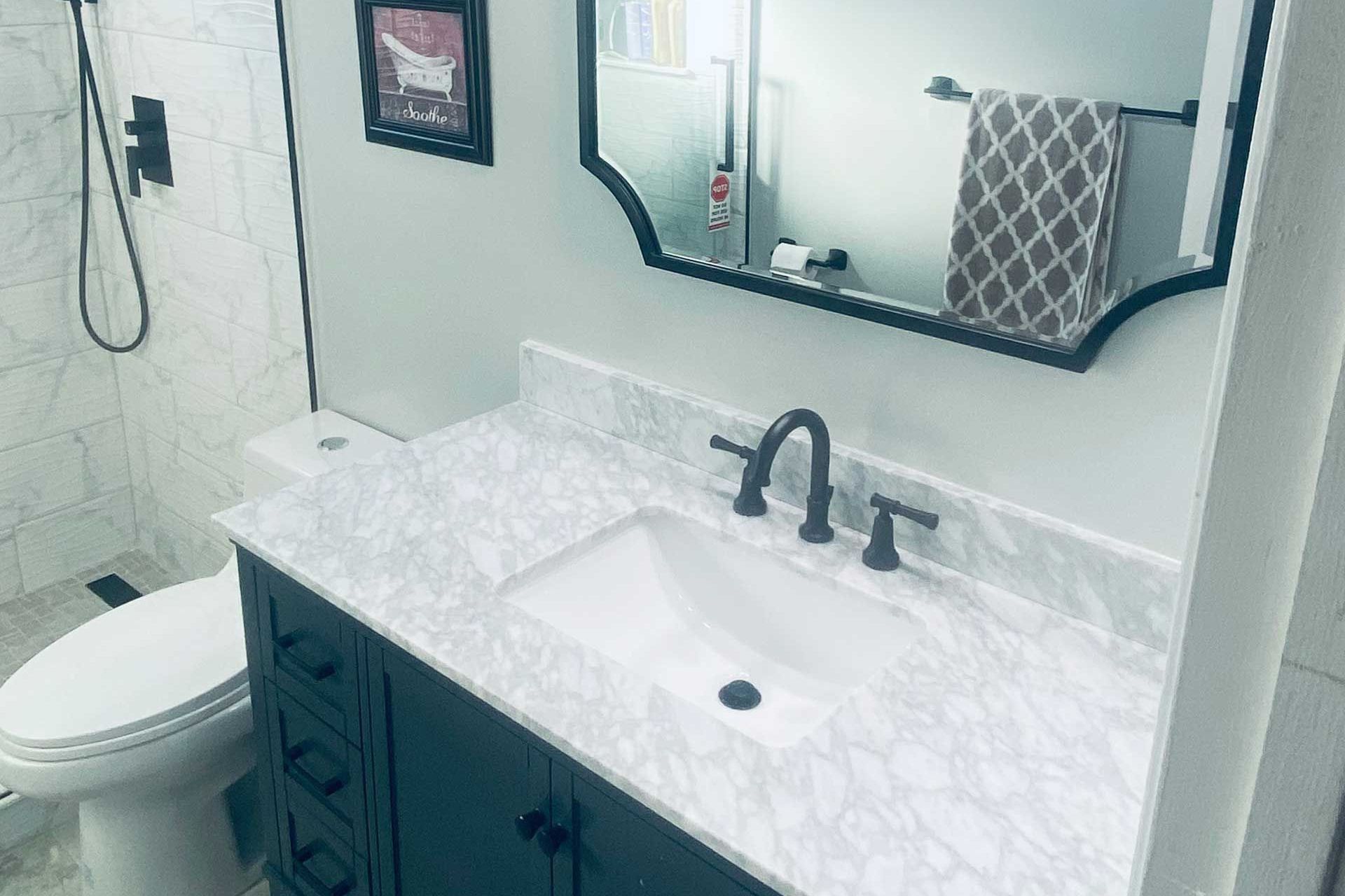 Bathroom with white marble countertop, dark vanity, black faucet, and decorative mirror. 
