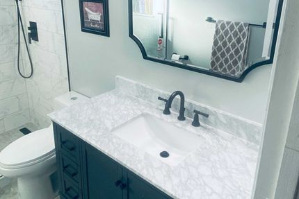 Bathroom with white marble countertop, dark vanity, black faucet, and decorative mirror. 