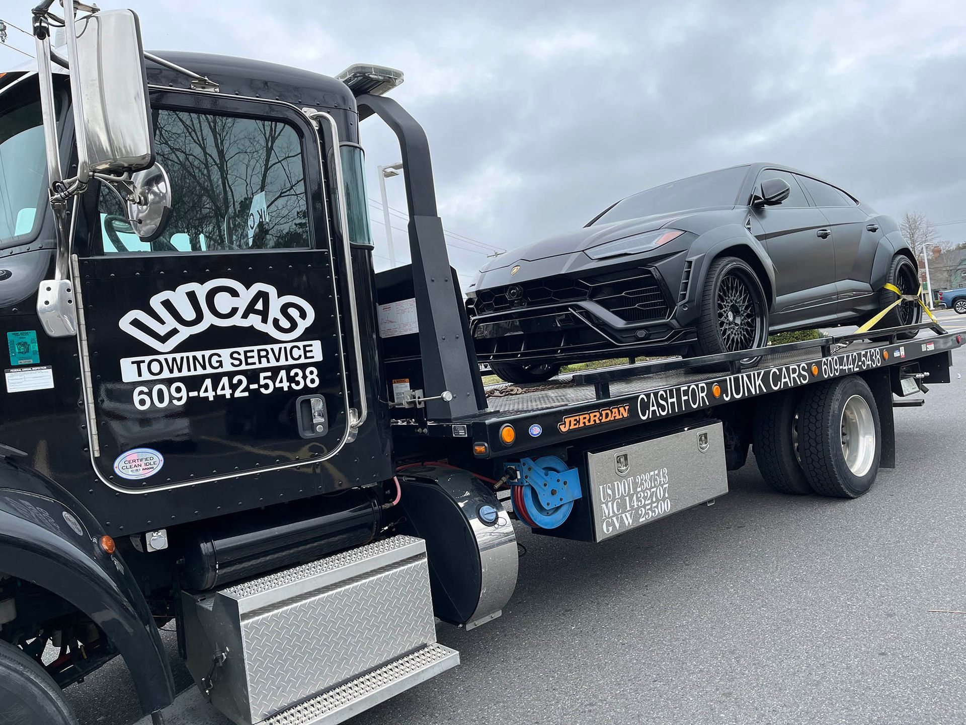 A black tow truck is towing a black car.