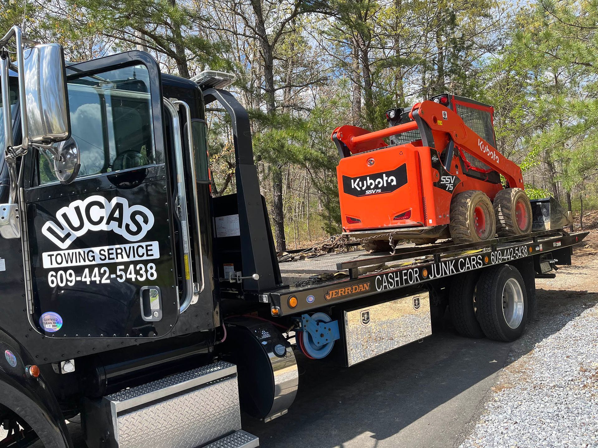 A tow truck is carrying a small tractor on the back of it.
