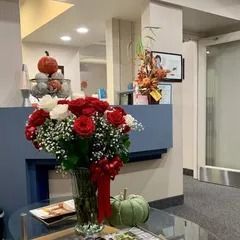 Lobby floral arrangement with red and white flowers, pumpkins, and a green gourd on a glass table.