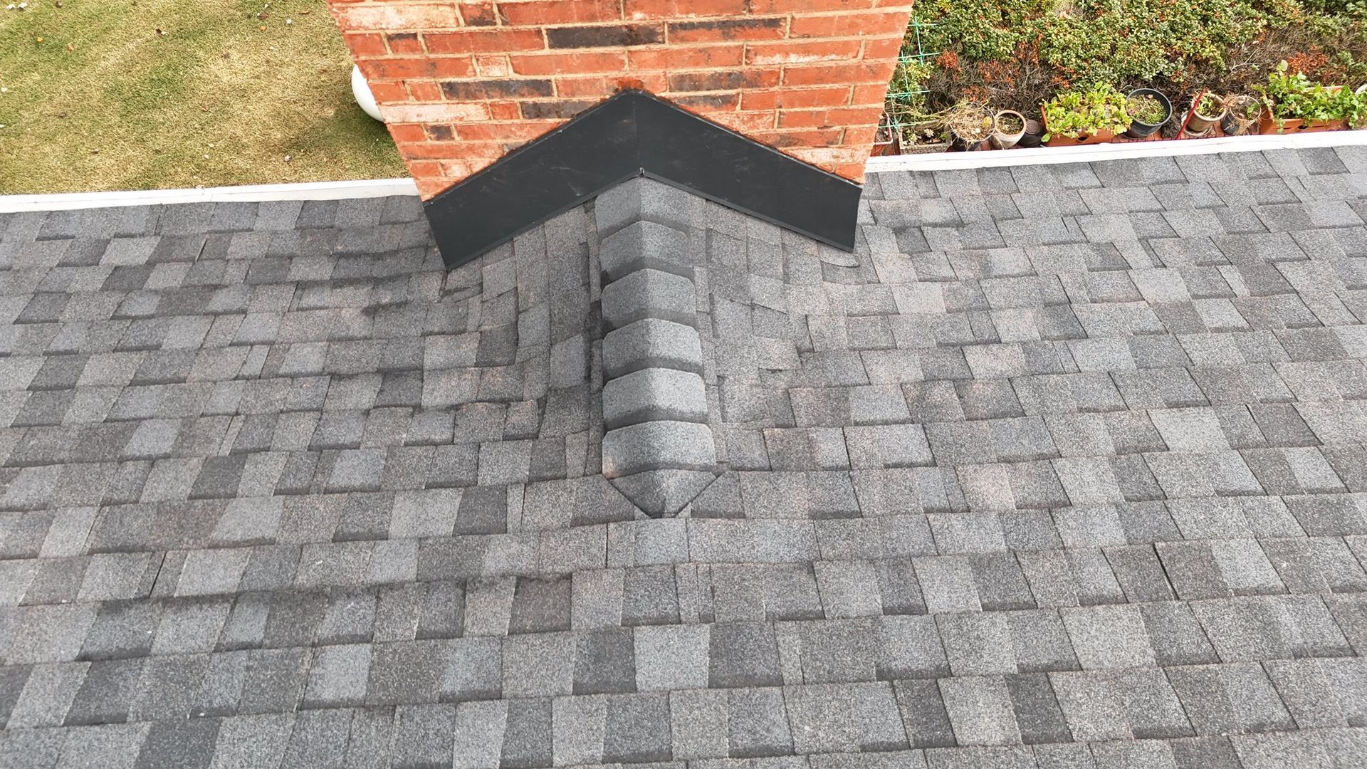 Gray shingle roof with brick chimney, black flashing, and green grass.