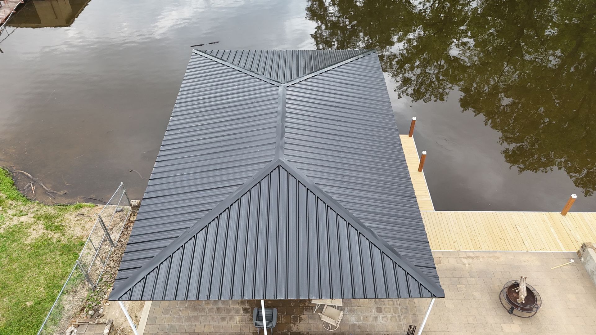 A gray, wavy-roofed boat dock with a wooden pier, next to murky water.
