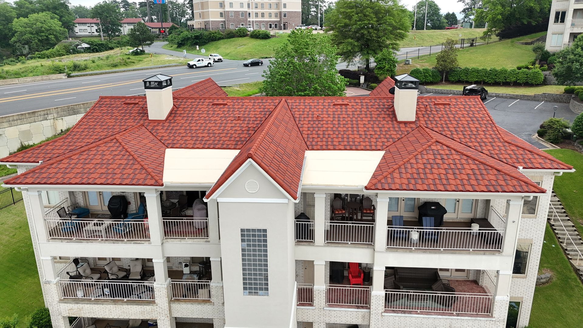 Multi-story building with a red tile roof, white walls, balconies, and people on the balconies.