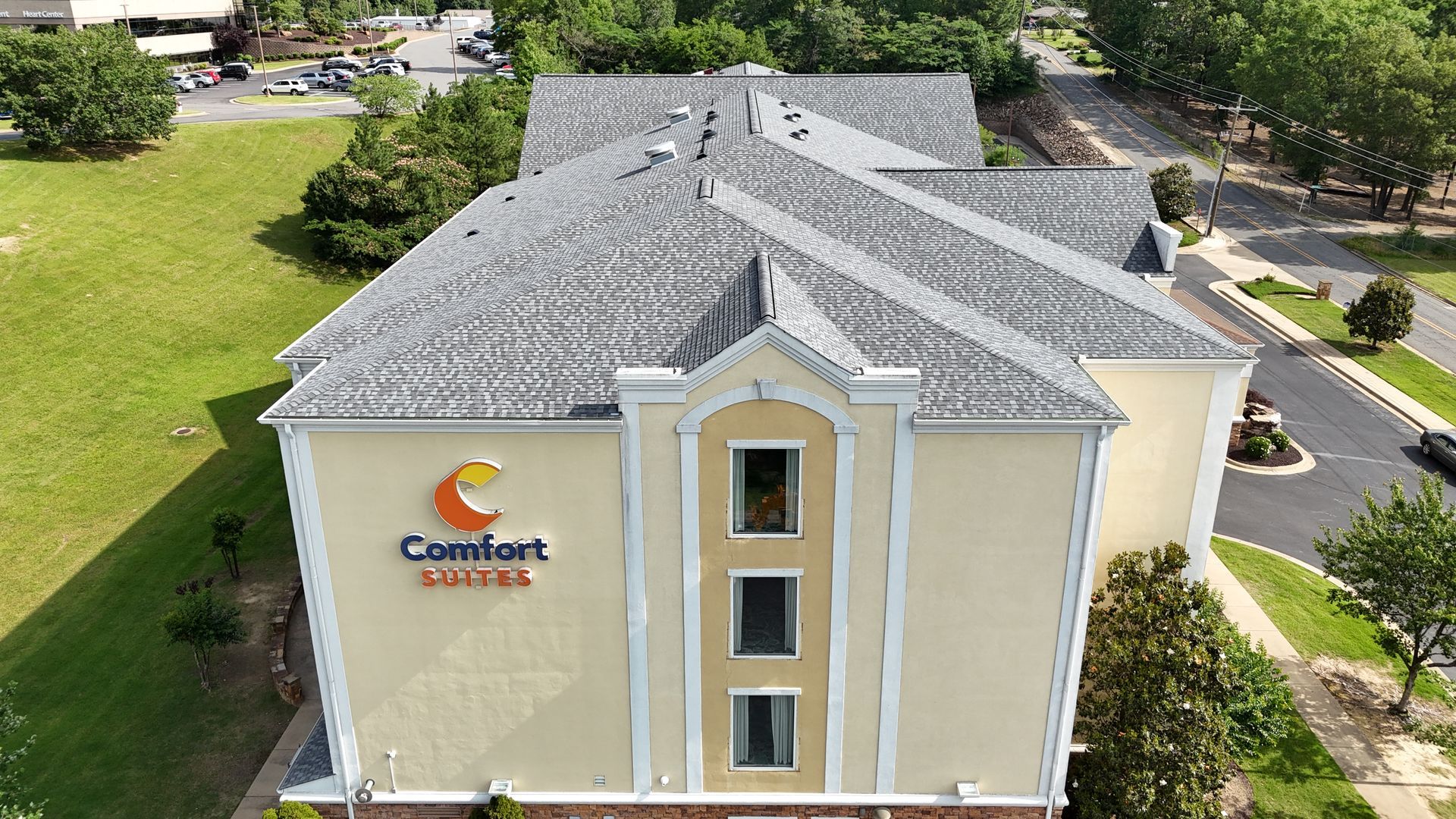 Comfort Suites hotel, exterior view, light yellow building with gray roof, green lawn, trees, and blue sky.