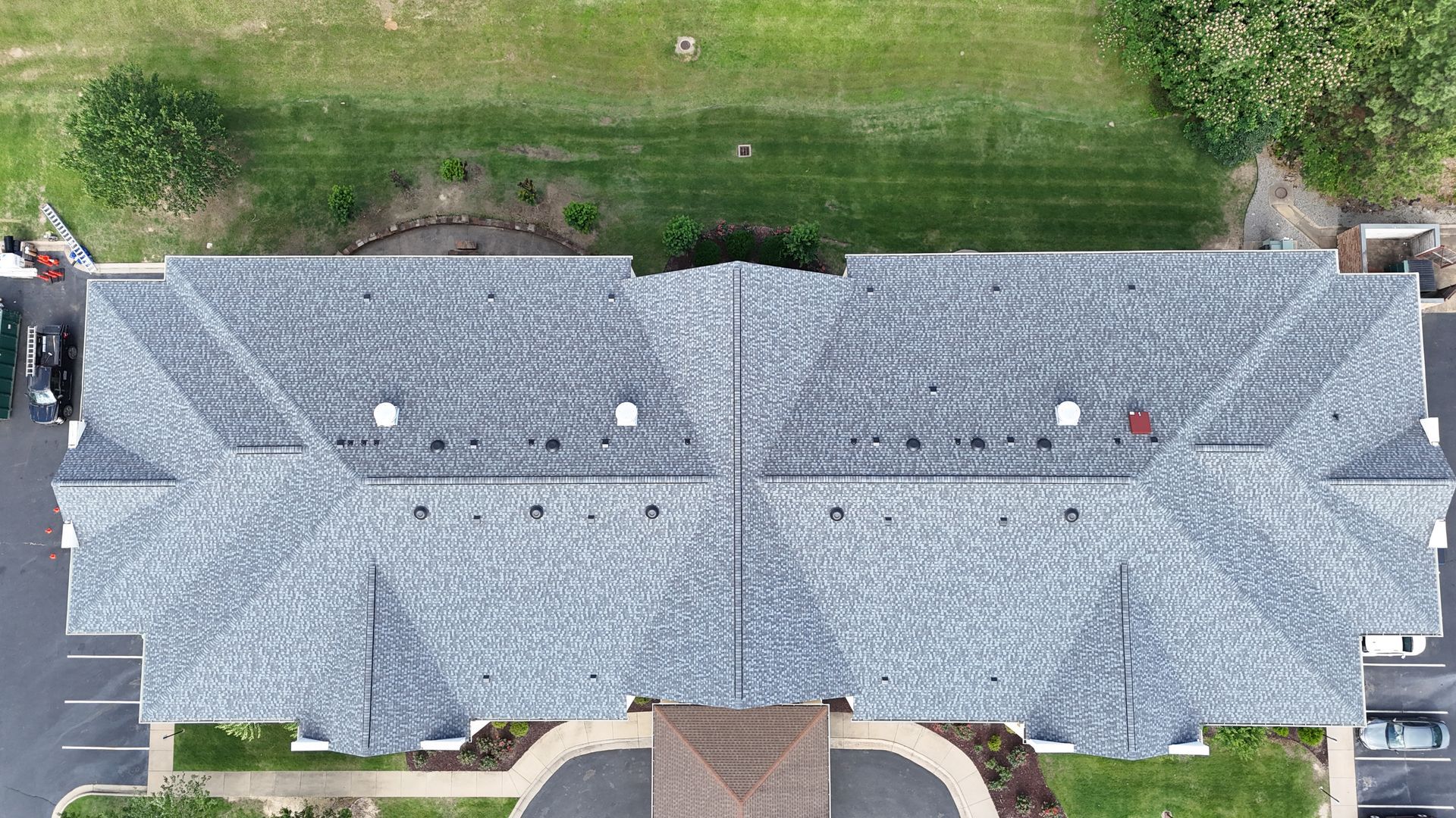 Overhead view of a gray shingled roof, part of a building with green lawn in the background.