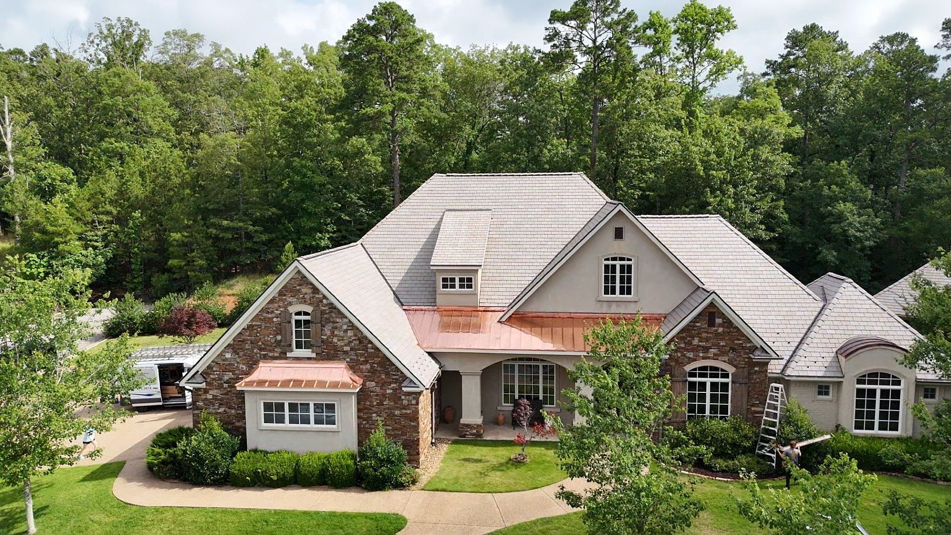 Stone and stucco house with copper accents and a cedar shake roof surrounded by trees.