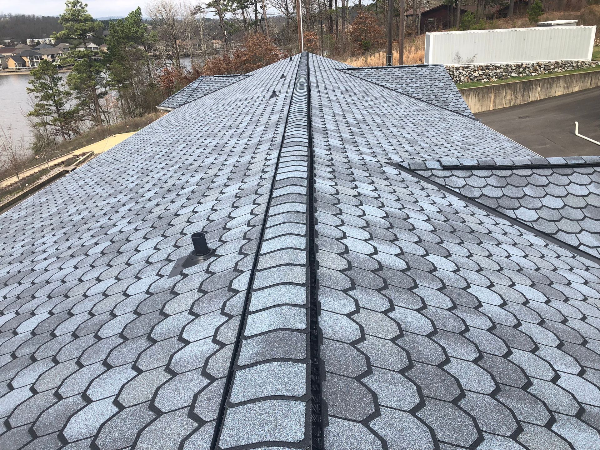 Gray scalloped shingles on a roof with a view of water and trees in the background.