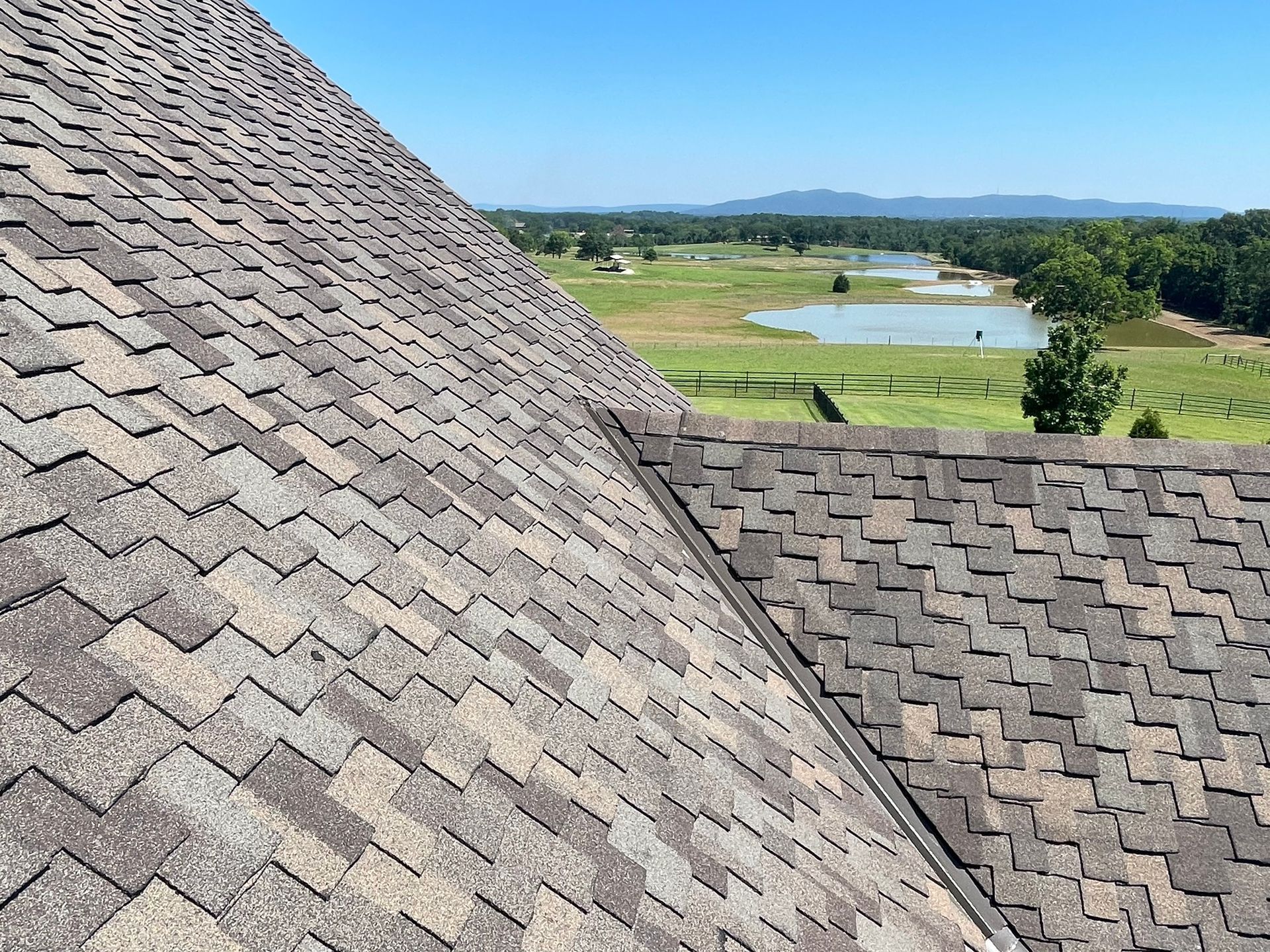 Close-up of a shingle roof with a scenic view of a lake and distant mountains on a sunny day.