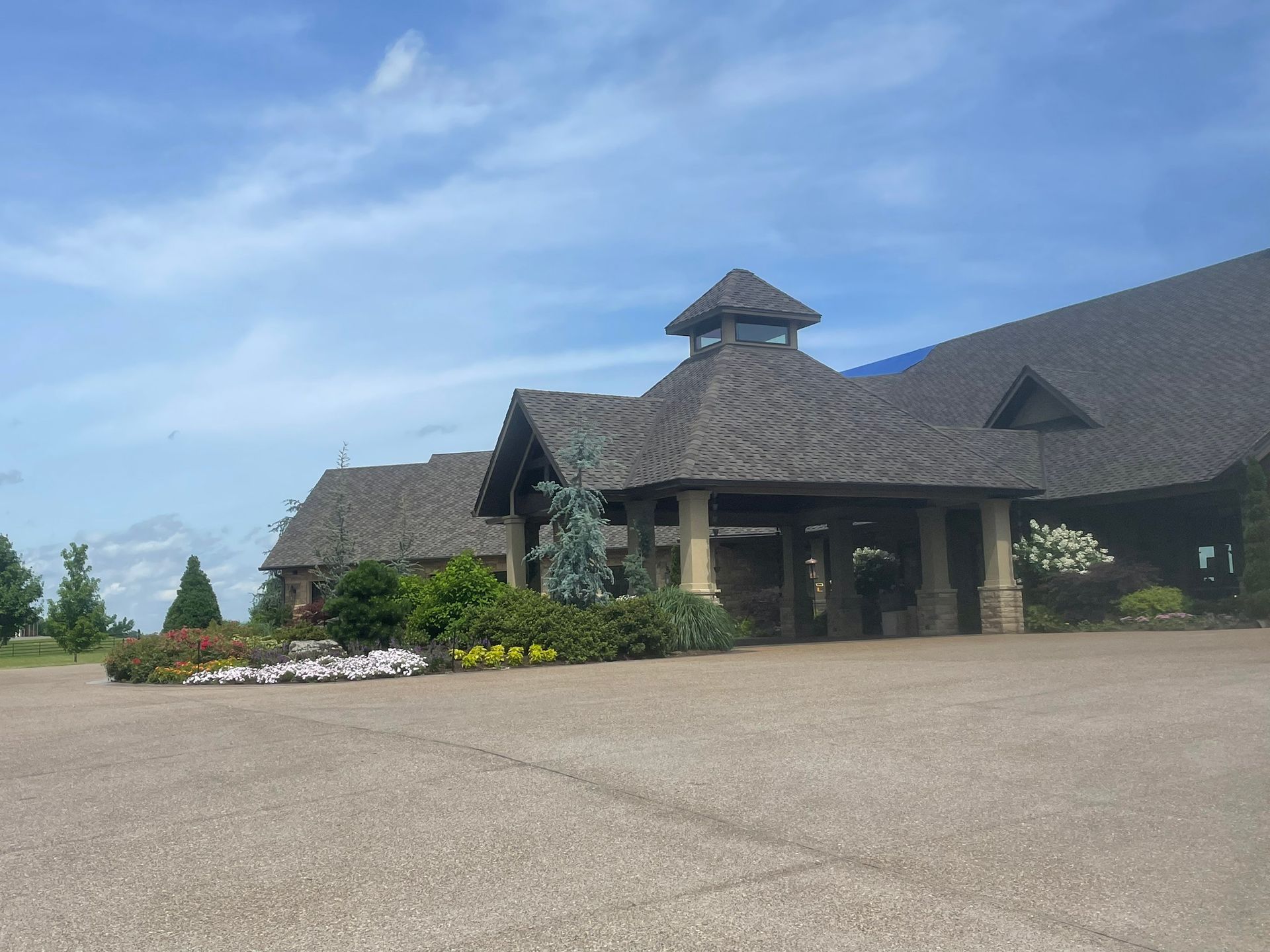 A large building with a covered entrance, surrounded by landscaping and a paved parking area on a sunny day.