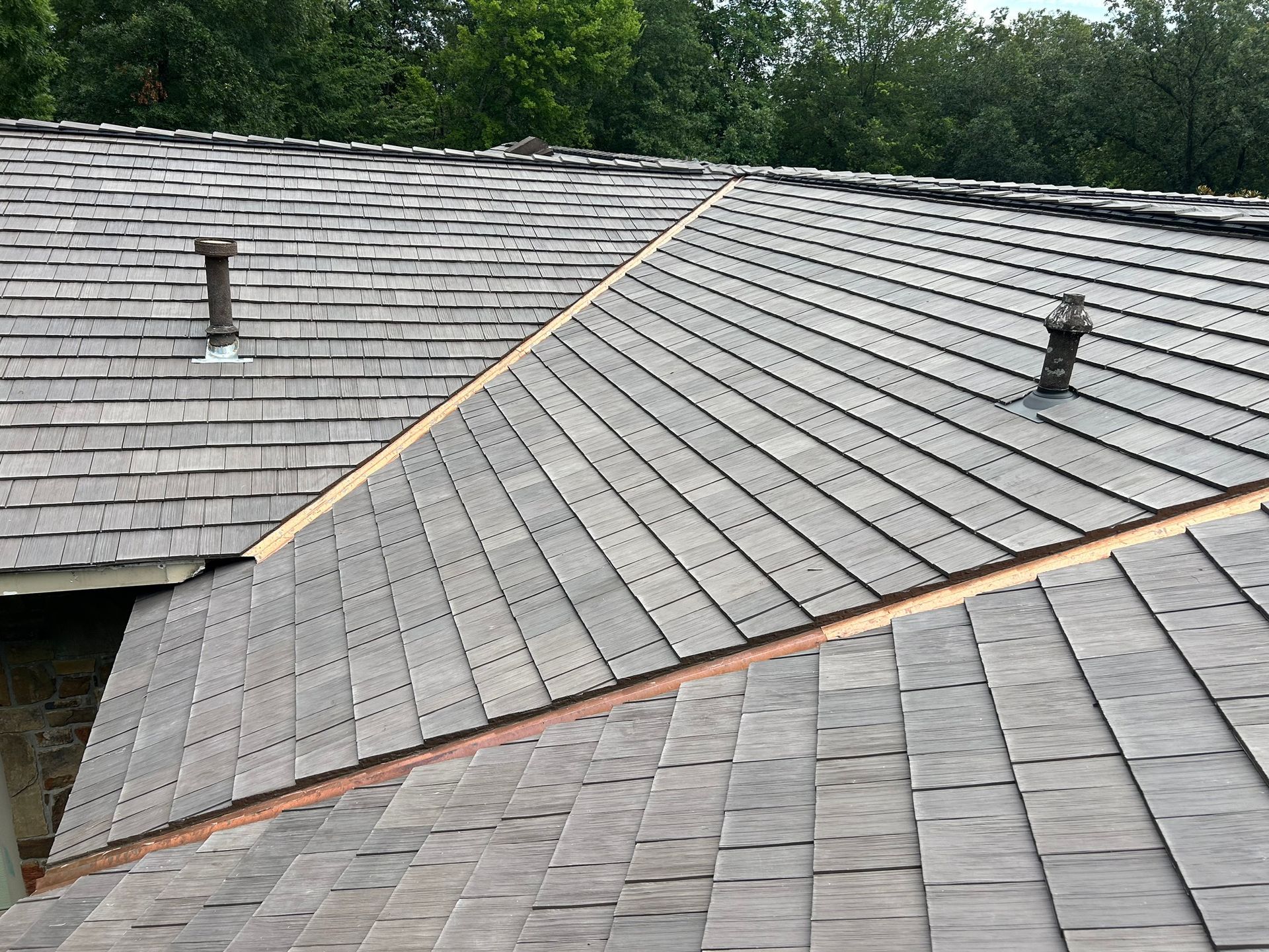 Gray wooden shingle roof with two vents, viewed from above on a sunny day.