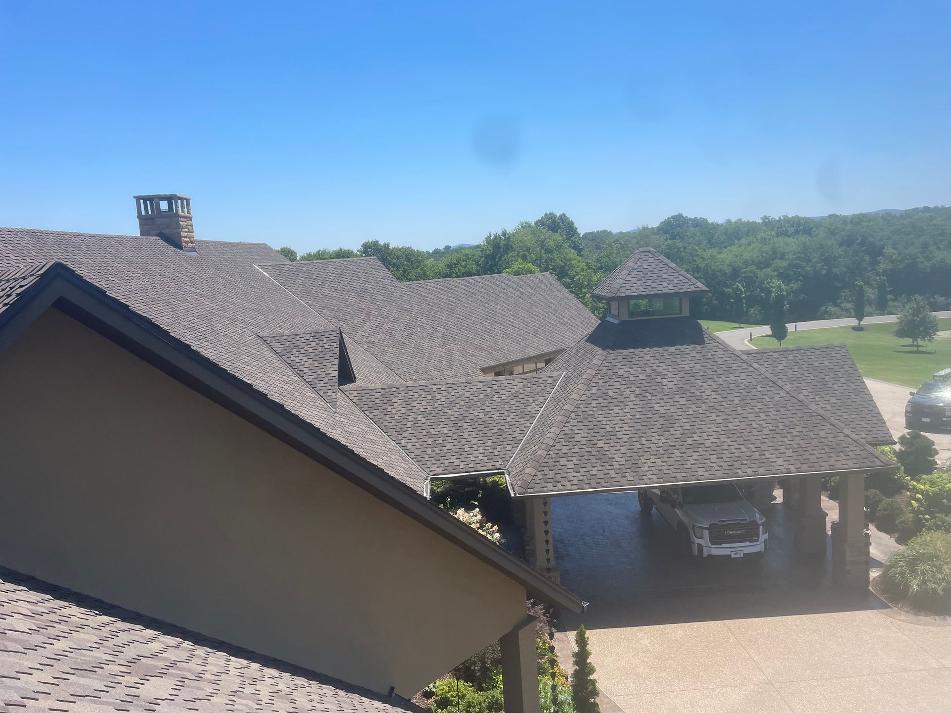View of a house with a dark roof, a covered car park, and a clear blue sky.