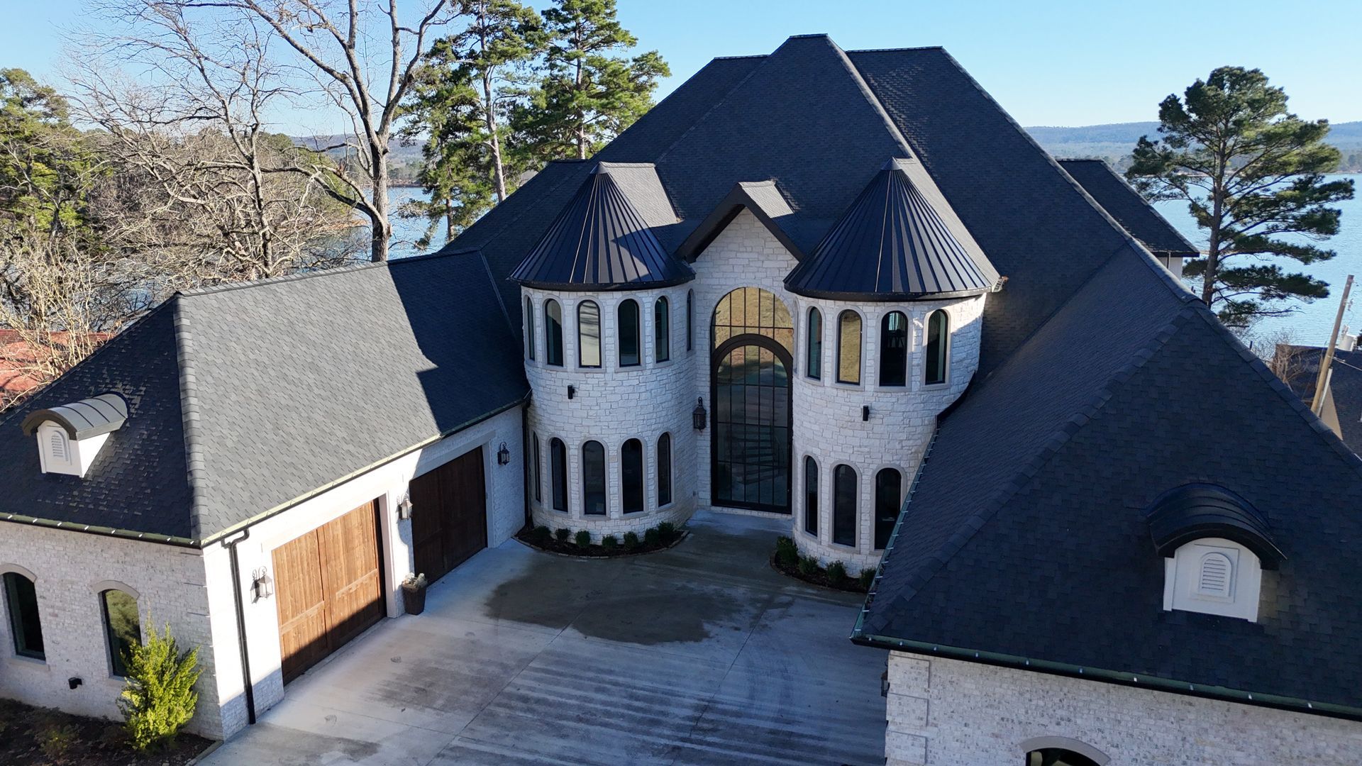 White brick mansion with dark roof, turrets, and a lake view.