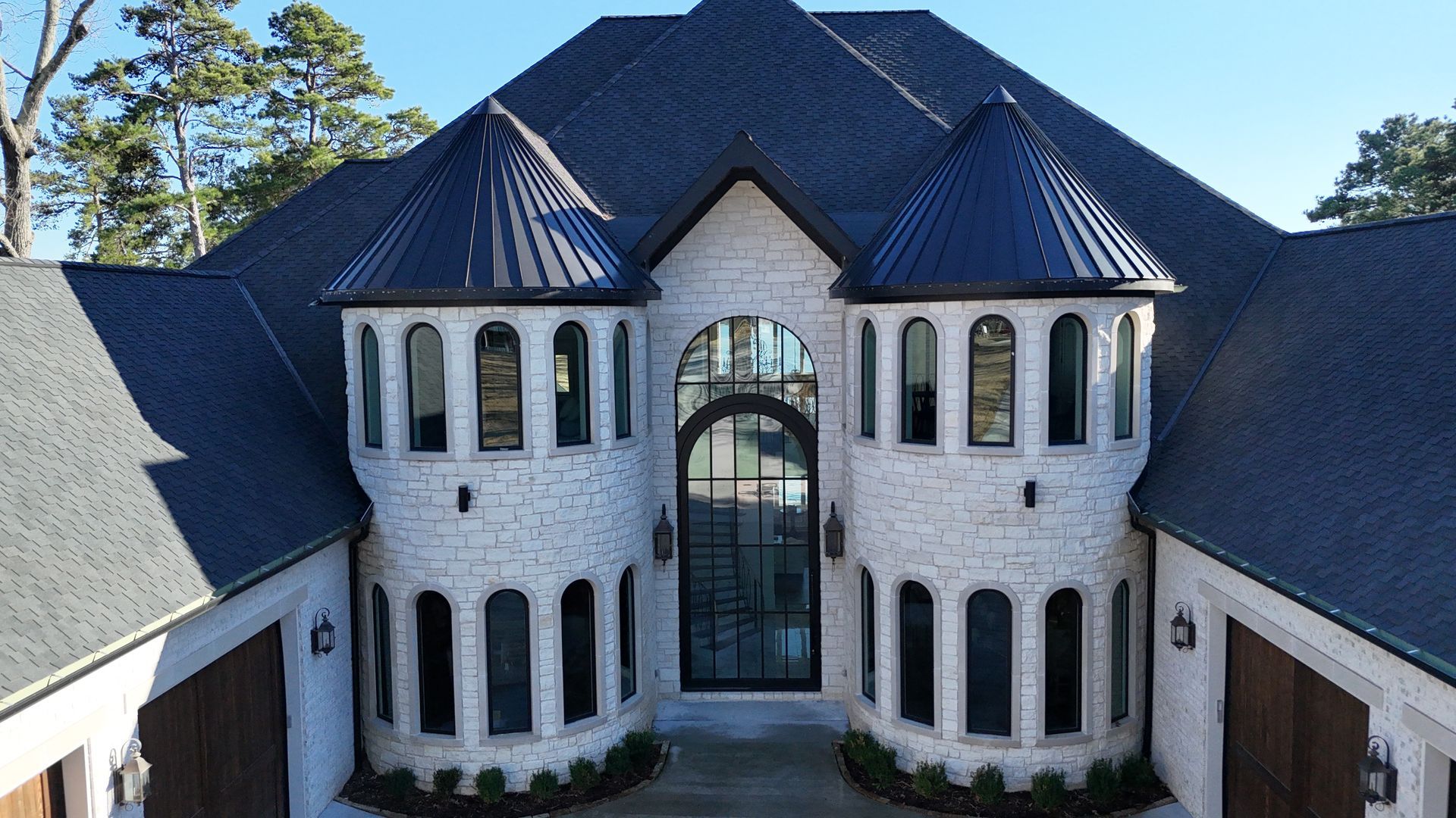 White brick mansion with black roof and turret, large black metal and glass front door.