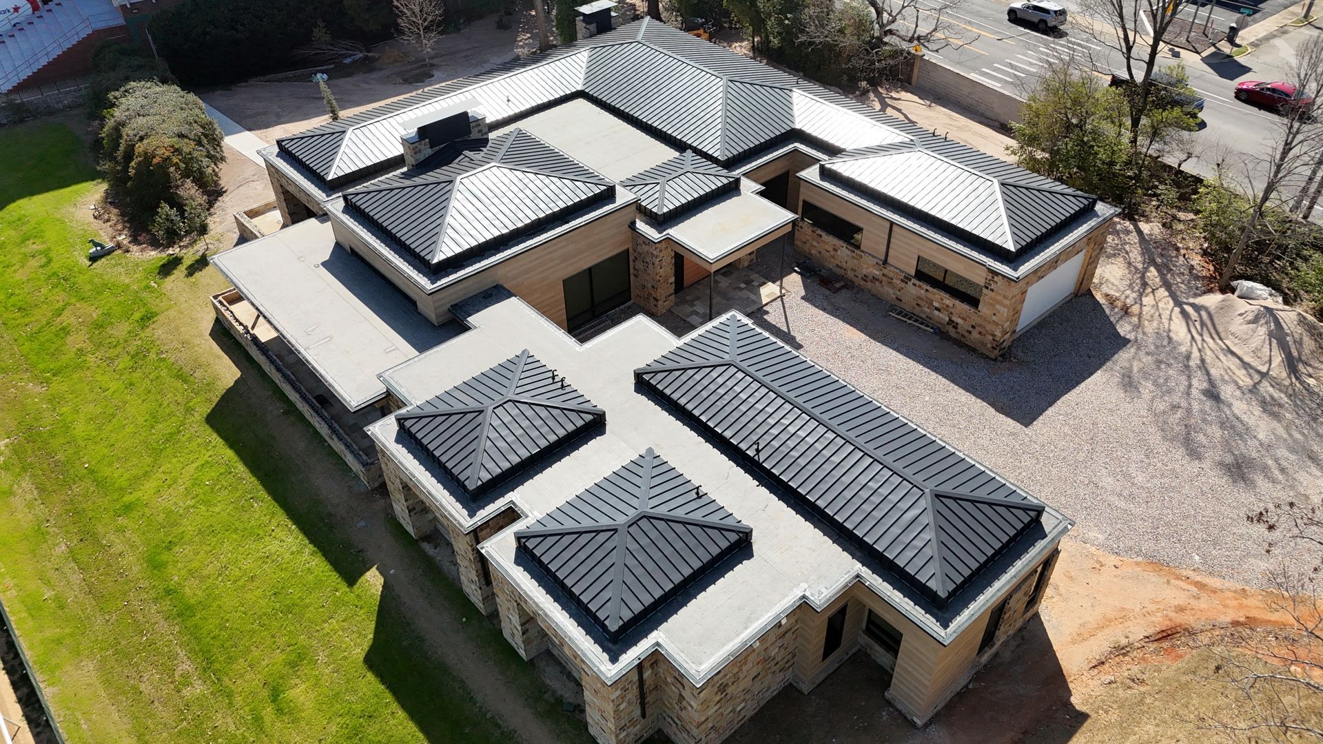 Aerial view of a modern, single-story home with a dark metal roof and light-colored stone exterior.